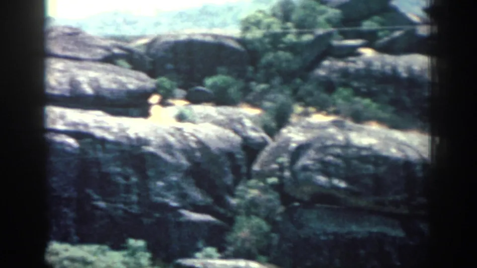 Rhodes landscape frame with broad rock shelves, scattered vegetation, bright daylight, and soft 8mm focus.
