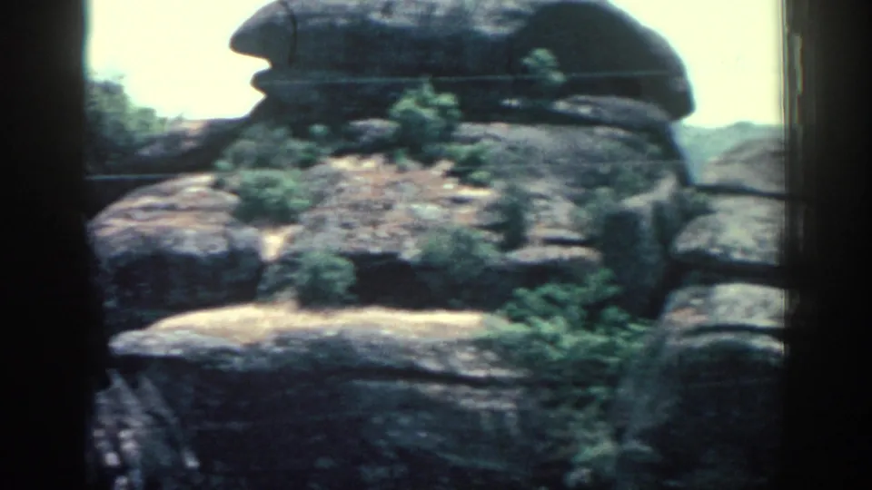 Vintage 8mm view of a rounded rock outcrop on Rhodes, with low shrubs and dry earth beneath.