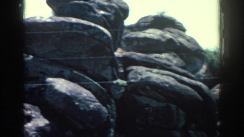 Soft 8mm frame of stacked Rhodes boulders, sparse shrubs, pale sky, and visible film-frame borders.