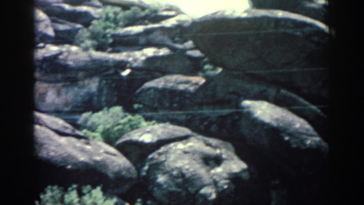 1962 Rhodes home-movie frame showing large weathered rocks and sparse greenery in a likely zoo enclosure.