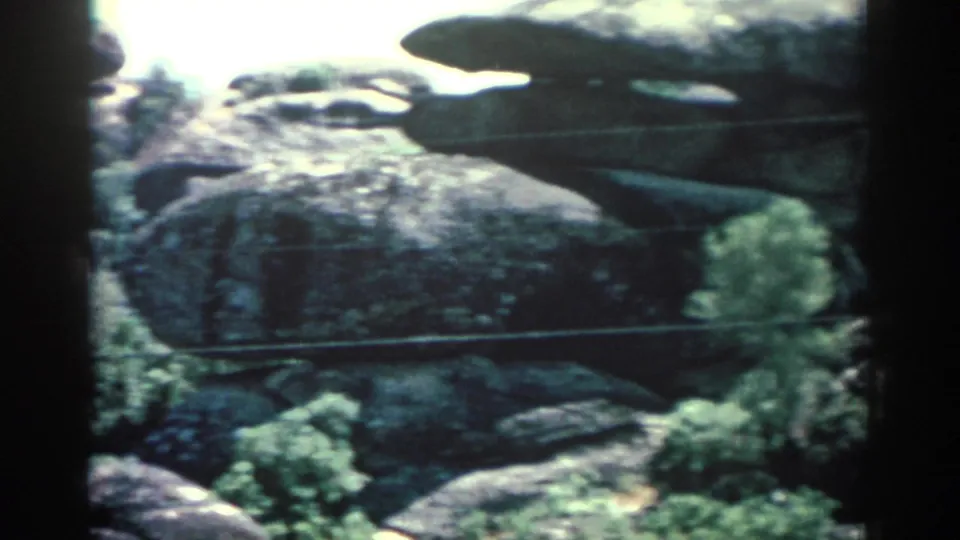 1962 8mm view of broad rock faces and vegetation, likely part of a zoo or wildlife-park enclosure in Rhodes.