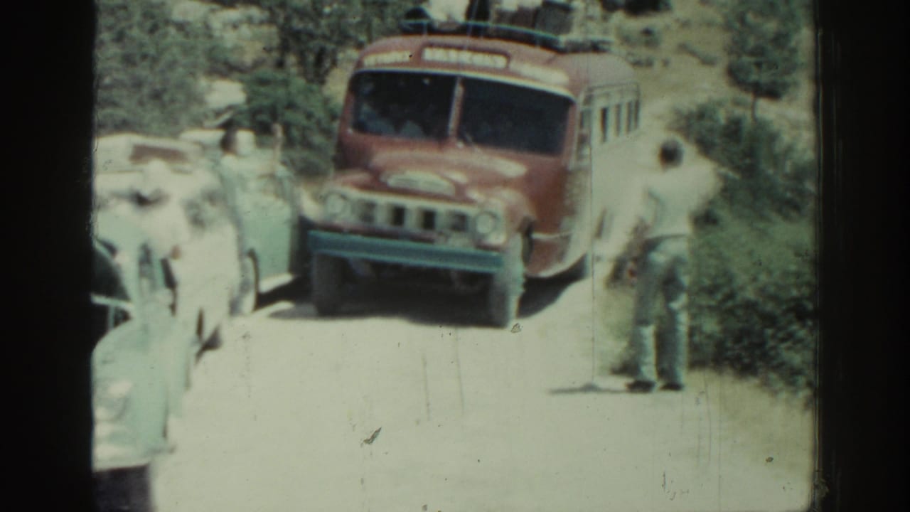 Red-and-white bus facing classic cars on a narrow road with people standing nearby.