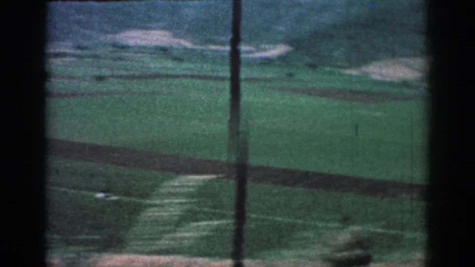 A moving 8mm travel view across Rhodes countryside, with green fields, hills, and dark window bars in the foreground.