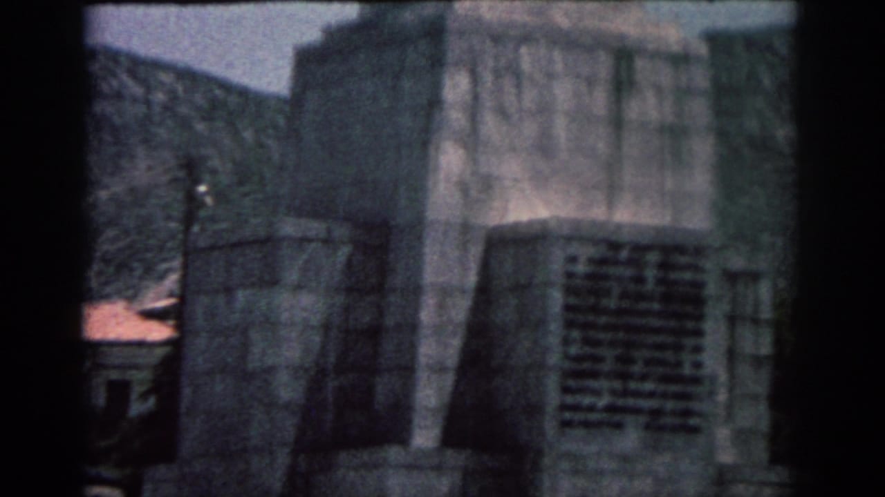 1962 Rhodes home-movie frame showing a grey stone monument base against rocky hills and pale blue sky.