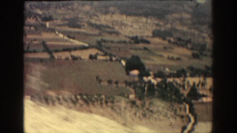 Wide 8mm Rhodes landscape view with fields, trees, small buildings, and a hillside in faded color.