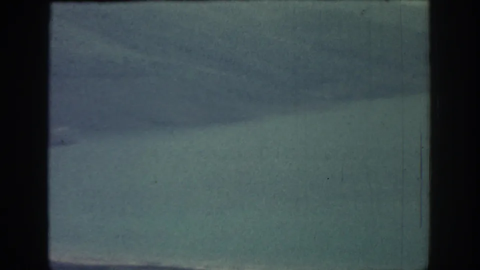 Faded 8mm frame from Rhodes showing broad blue-green water, hazy hills, cloudy sky, and the horizontal boundary of the contact-sheet frame.