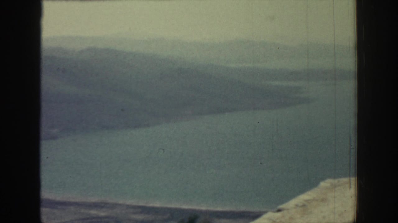 Hazy sea and distant hills seen above a pale rocky foreground.
