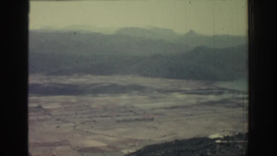 Rhodes landscape frame from 1962 showing flat sandy ground or fields leading to water and misty mountains, with visible 8mm wear.