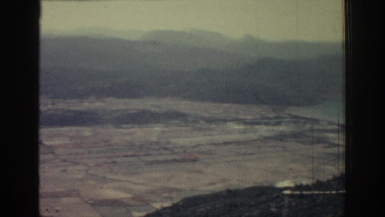Hazy aerial view of tan fields and distant mountains framed by dark vertical edges.