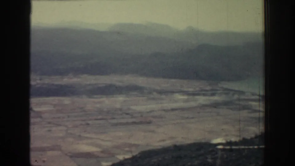 1962 Rhodes home-movie frame showing tan fields, distant mountains, haze, and dark window-like borders.