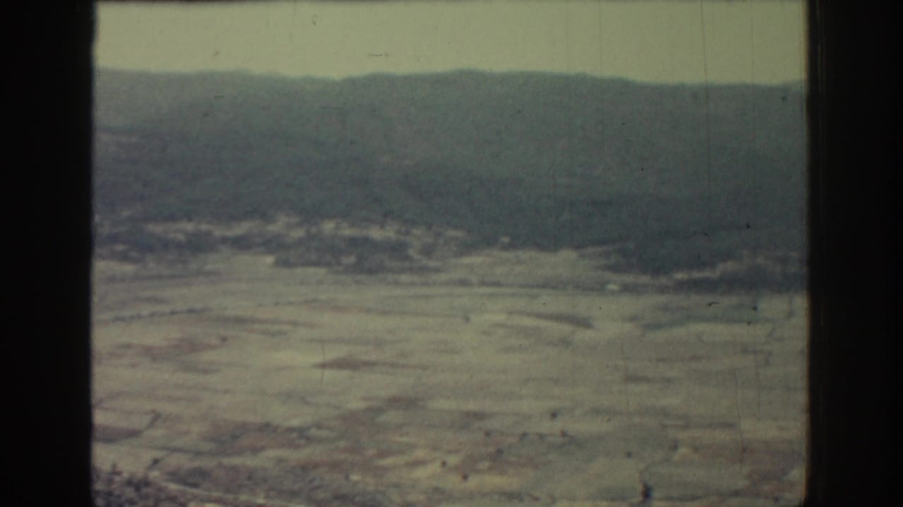Wide aerial view of barren fields and low hills with visible film gate edge.