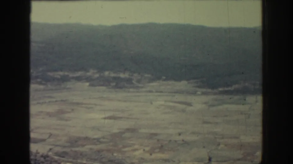 1962 Rhodes aerial frame with muted fields, a low hill line, faint tracks, and the dark vertical edge of the film frame.