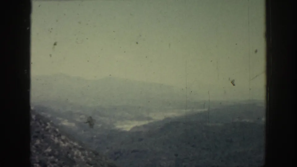 1962 Rhodes home-movie view of a hazy hillside landscape, with distant water barely visible through the fog.