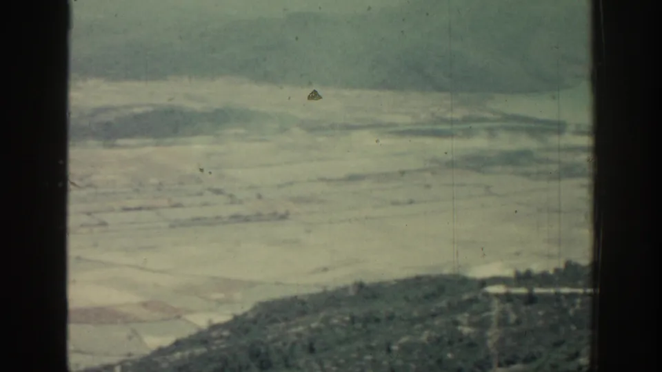 1962 Rhodes coastal frame with distant pale shoreline, blue-green water, low hills, and dark 8mm frame borders.