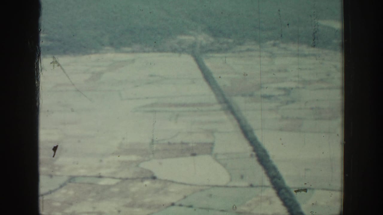 Aerial view through dark window bars over pale patchwork fields and low hills.
