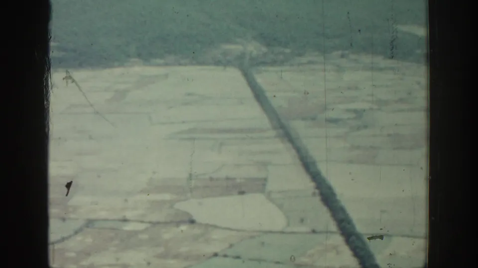 1962 8mm aerial view over Rhodes, Greece, with dark aircraft window bars framing pale fields and distant hills.