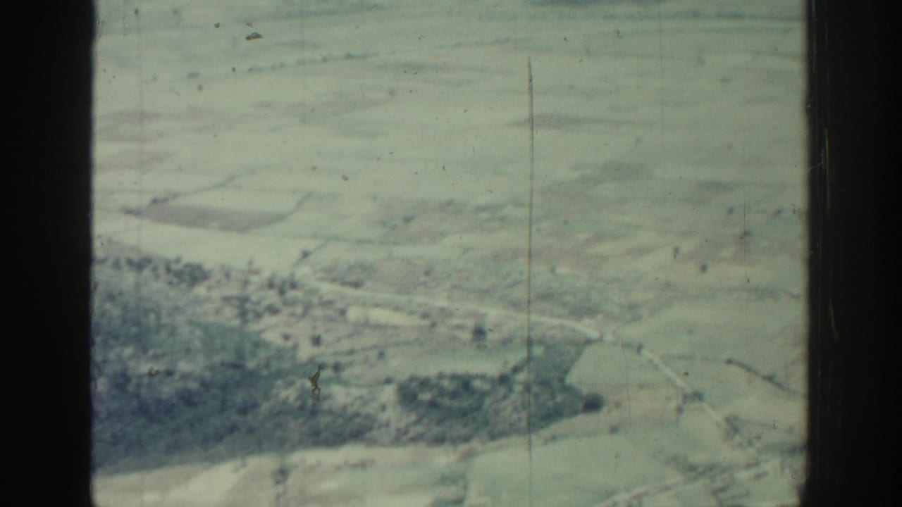 Aerial view of fields and wooded terrain seen through a dark window frame.