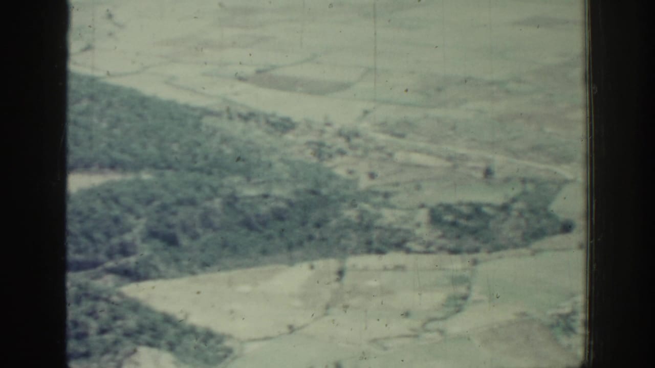 Aerial view of wooded hills, fields, and scattered buildings beyond a window frame.