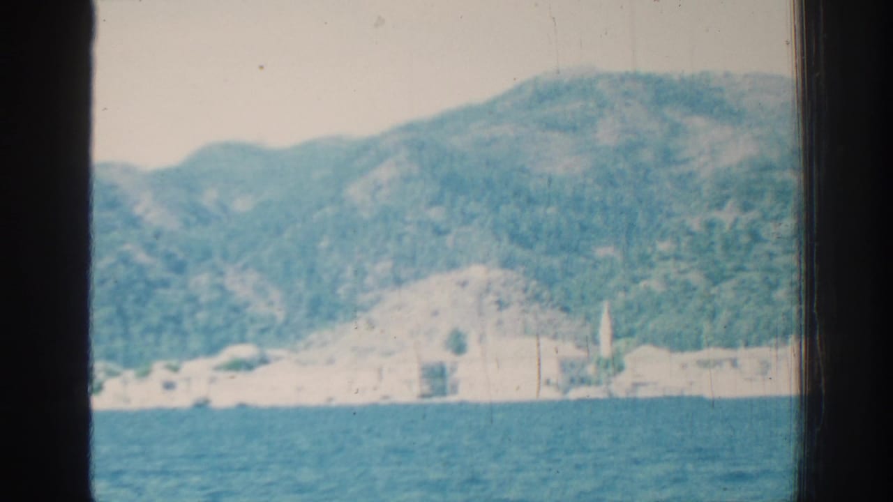 Blue water with a distant pale shoreline and wooded mountains behind dark frame edges.