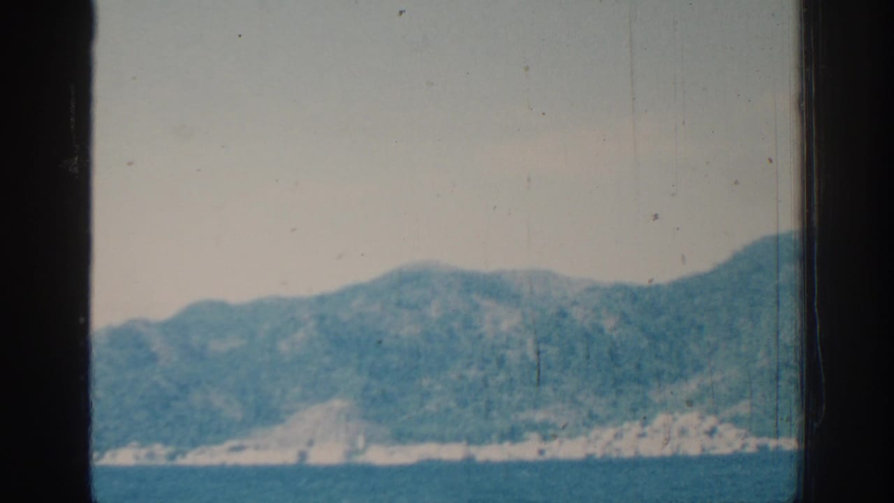 Hilly shoreline and blue water seen through dark vertical framing, with soft faded color.
