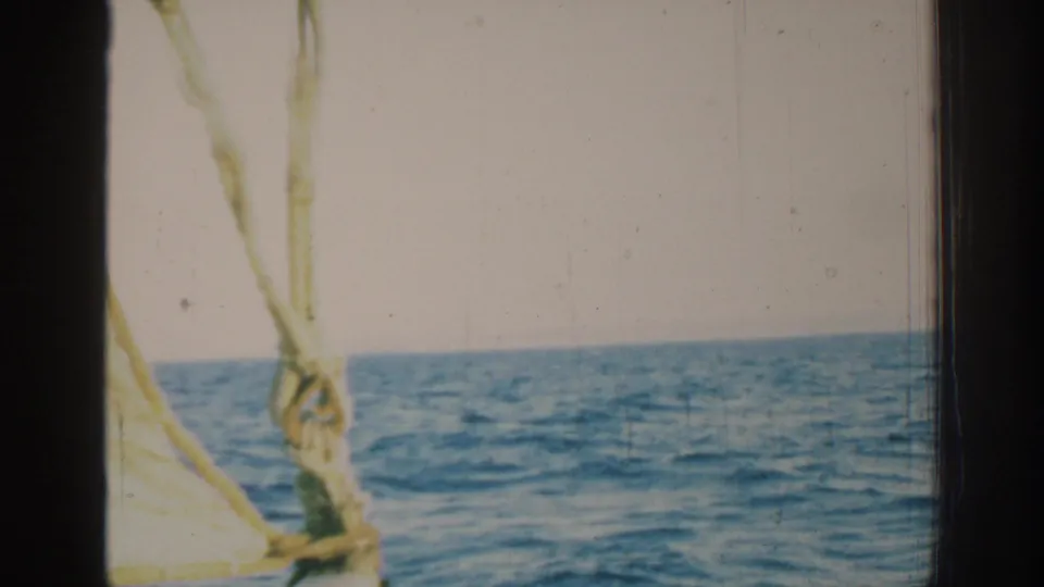 Shipboard 8mm view near Rhodes in 1962, with rope rigging and sail detail against open blue water and sky.