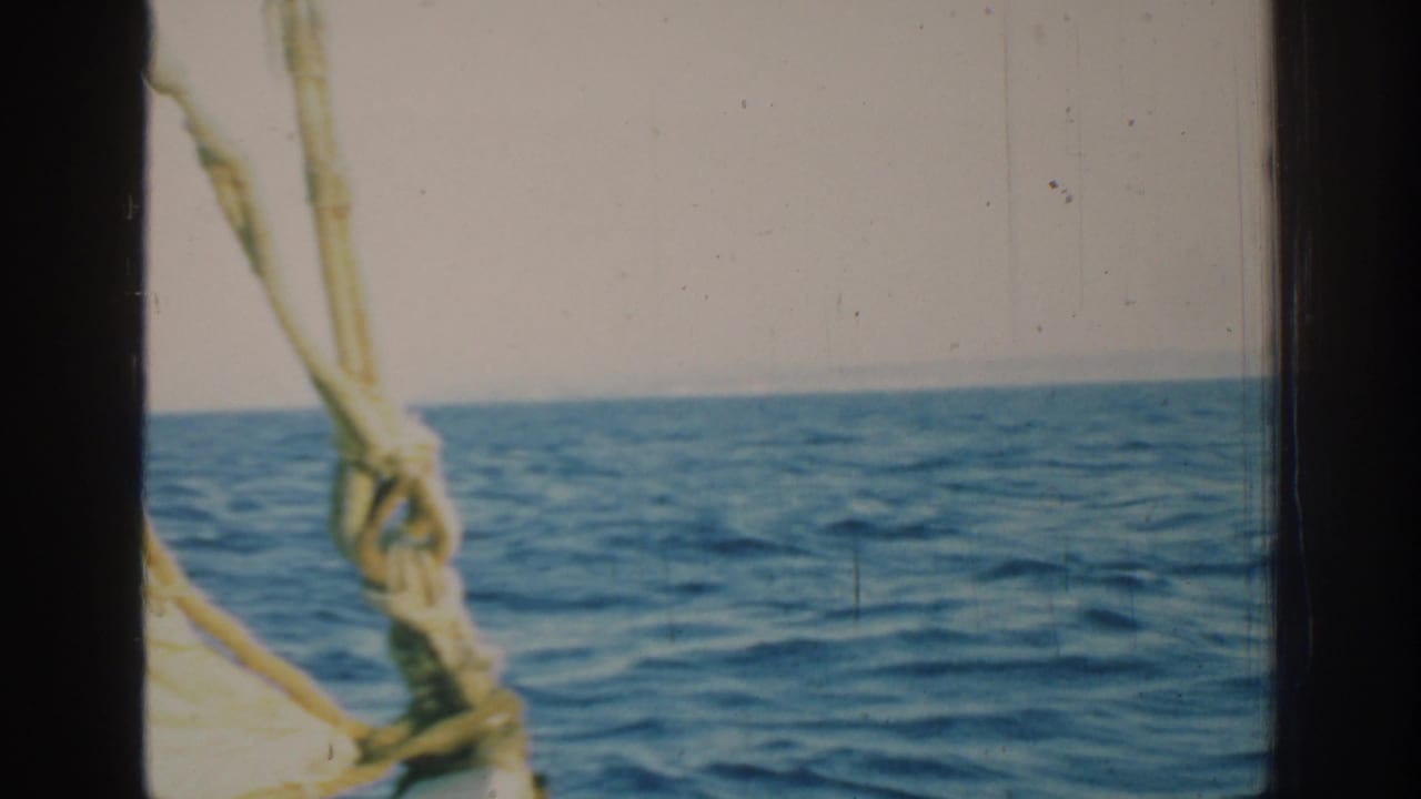Blue sea and hazy horizon seen past dark boat framing and rope rigging.