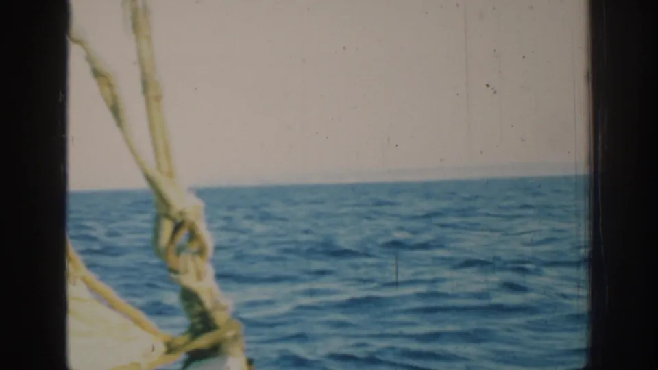 1962 8mm view from a sailboat near Rhodes, Greece, with blue water, pale sky, dark frame edges, and rope rigging.
