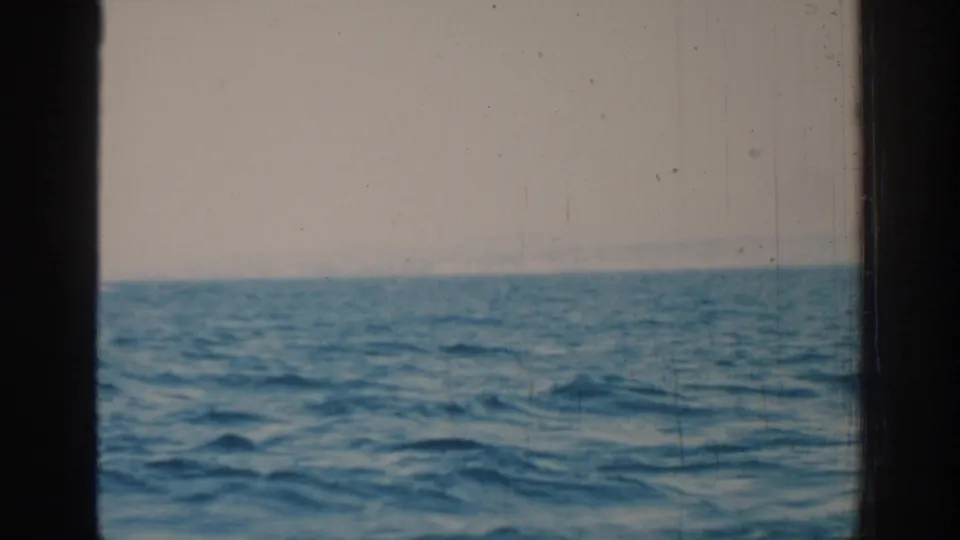 A 1962 8mm sailboat view near Rhodes shows rippling blue sea, pale sky, distant haze, and dark vertical framing.