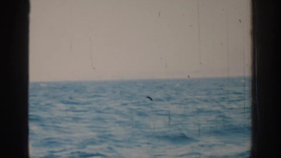 1962 Rhodes 8mm frame showing choppy blue water under a pale sky, viewed through dark boat-window or frame edges.