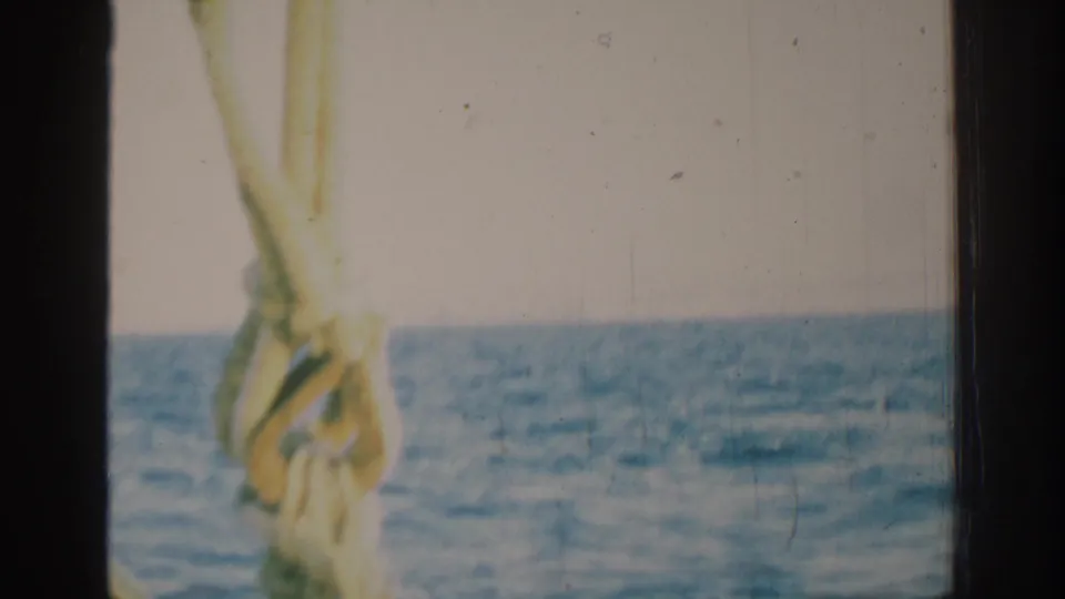 1962 Rhodes boat view with blue water, pale cloudy sky, a dark central divider, and a light rope or line in front.