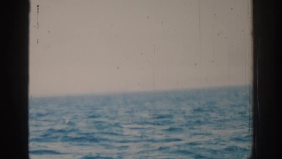 1962 Rhodes 8mm frame of the sea from a moving boat, with dark framing and a pale cloudy sky above the horizon.