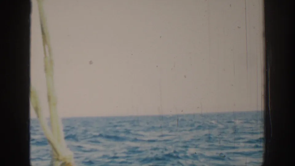 1962 8mm home-movie view near Rhodes, Greece, showing open water, pale sky, dark frame edges, and boat rigging at left.