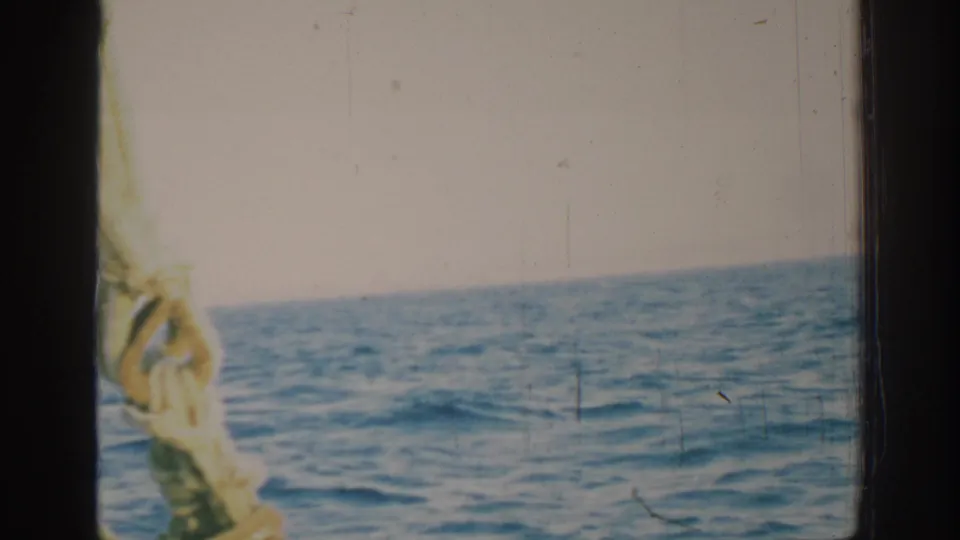 8mm home-movie frame from 1962 near Rhodes, Greece, showing choppy sea, pale sky, dark gate edges, and sailboat rope.