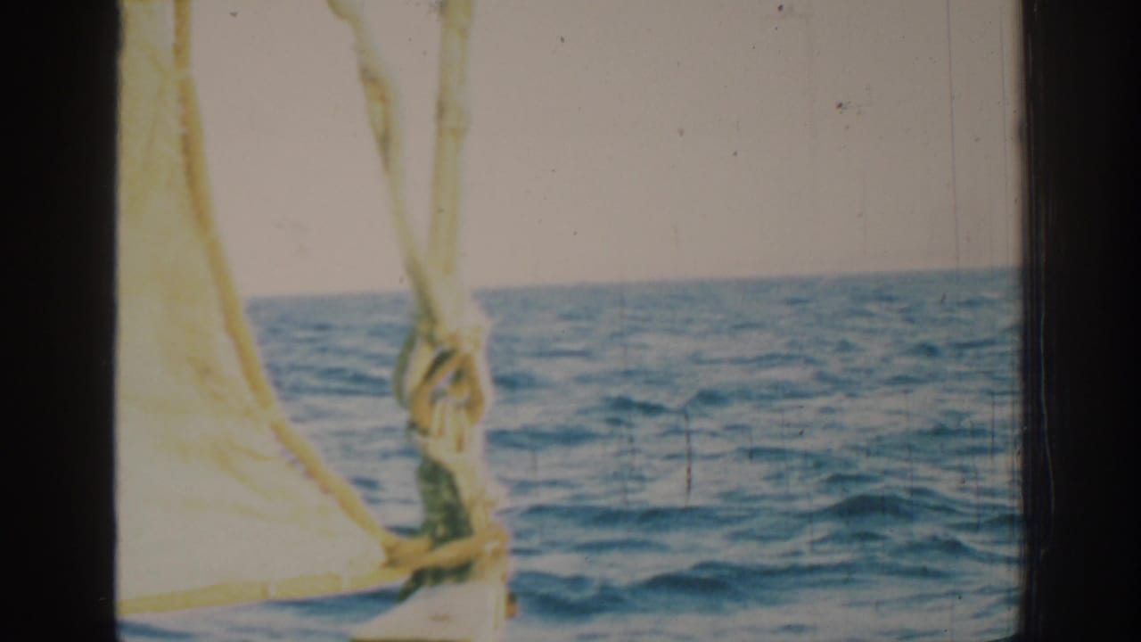 Blue ocean horizon seen past yellow sail cloth and rigging on an 8mm film frame.