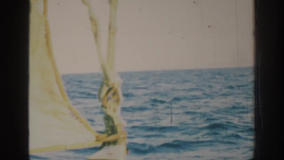 1962 Rhodes home-movie frame showing open blue water from a sailing vessel, with yellow sail cloth and rigging in the foreground.