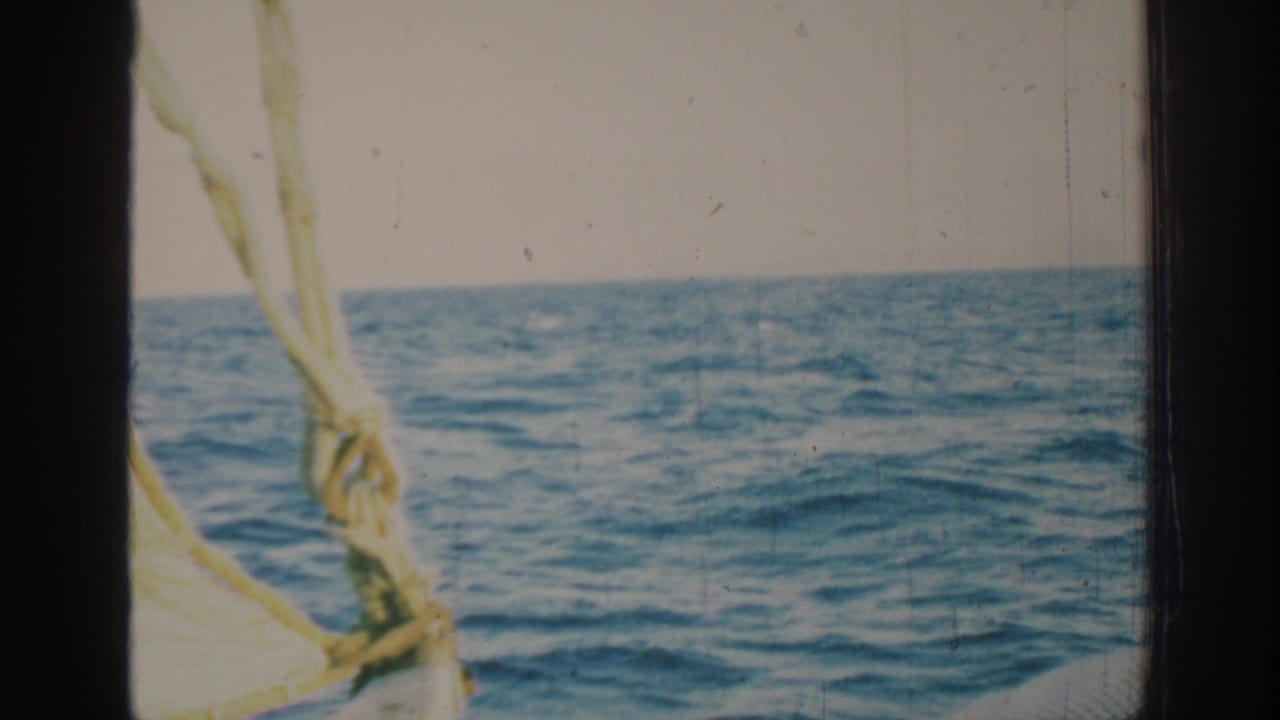 1962 Rhodes sailing view with blue Mediterranean water, a low horizon, pale sky, sail rigging, and visible 8mm film wear.