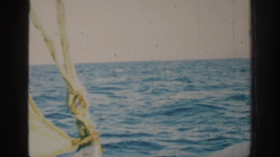1962 Rhodes sailing view with blue Mediterranean water, a low horizon, pale sky, sail rigging, and visible 8mm film wear.