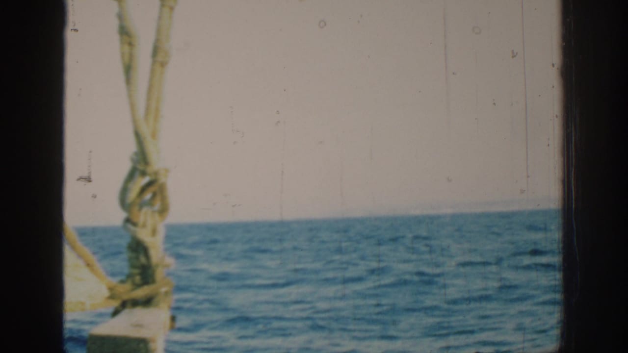 Open sea seen through boat rigging with a sail edge at left and dark film gate borders.