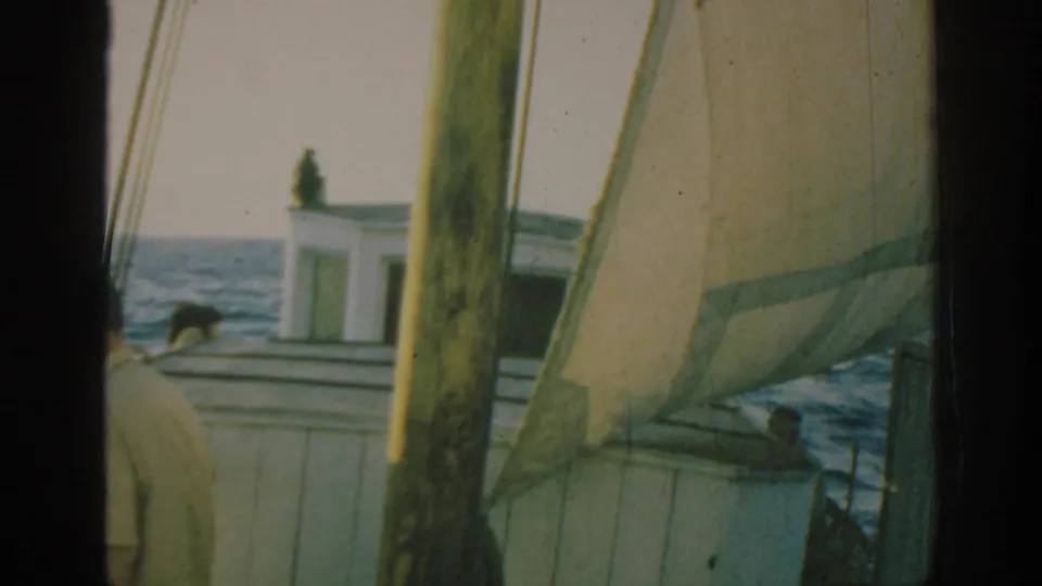 1962 Rhodes 8mm frame showing a sailboat deck, cabin, mast, sea horizon, and partially visible people aboard.