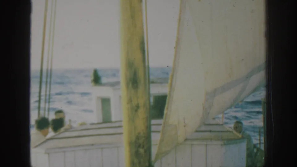 1962 Rhodes frame of a small sailboat under sail, with men on deck and the blue sea visible through the 8mm frame edges.