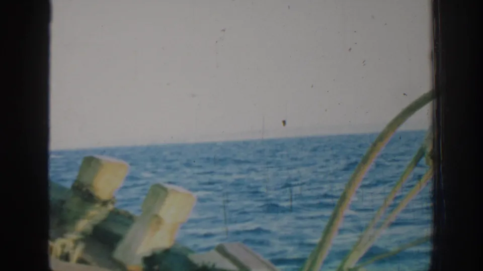 1962 Rhodes, Greece boat-view frame showing the blue sea horizon, pale sky, dark vertical borders, and foreground vessel hardware.