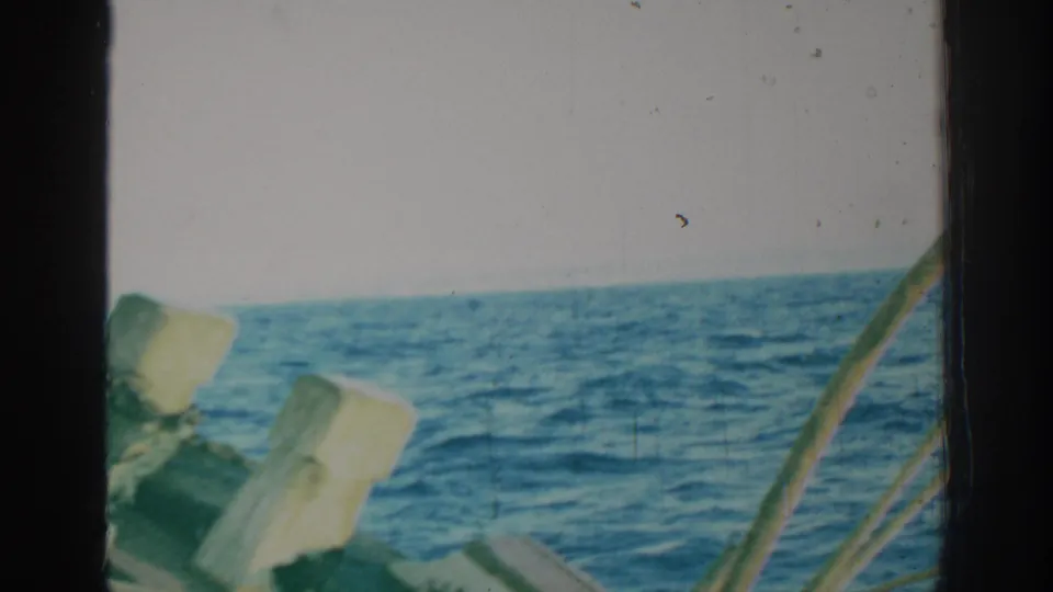 1962 Rhodes, Greece 8mm frame with rippling blue sea, pale sky, a dark window or cabin edge, and foreground railings.