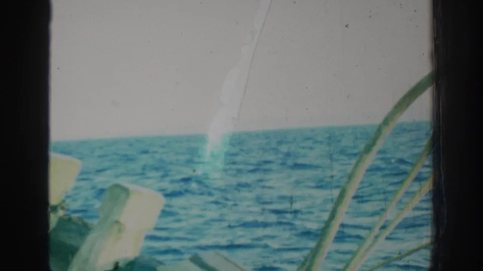 1962 Rhodes, Greece sea view from a vessel, with foreground railings, dark frame edges, and a bright vertical film mark over the water.