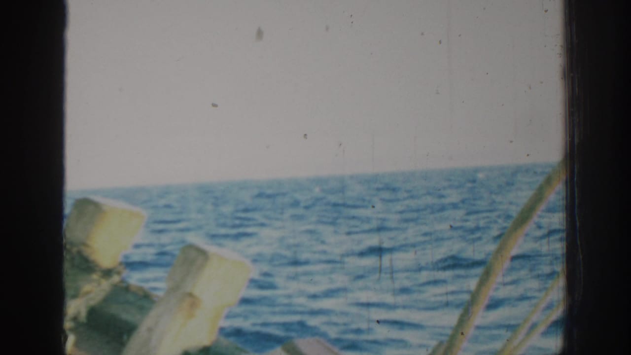 Open sea seen through dark film-frame edges and wooden boat posts.