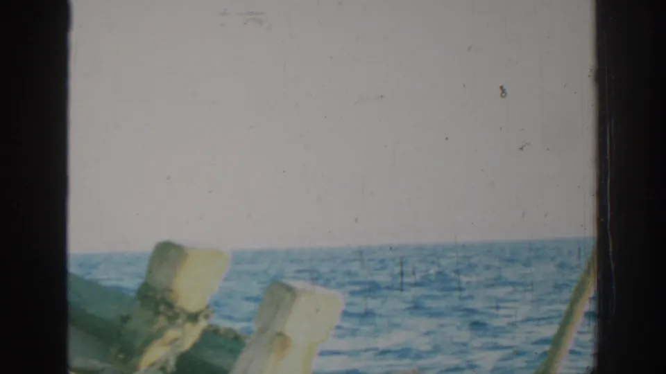 Faded 8mm frame of the Rhodes sea horizon, with weathered wooden boat posts crossing the lower foreground.