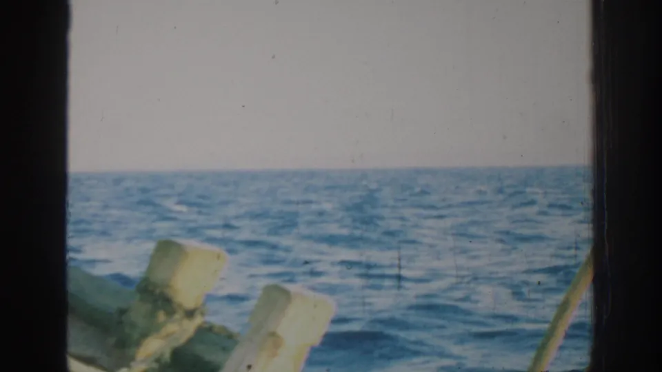 1962 Rhodes 8mm travel frame with open Mediterranean water, a pale horizon and boat rail posts near the camera.