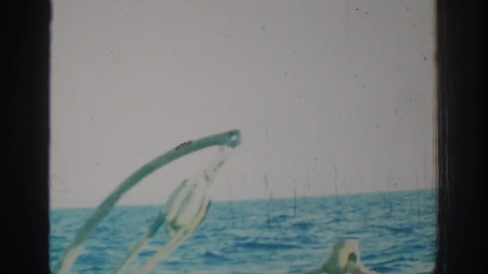 1962 Rhodes home-movie still with a bright sea horizon, curved boat hardware, rigging and visible 8mm film wear.