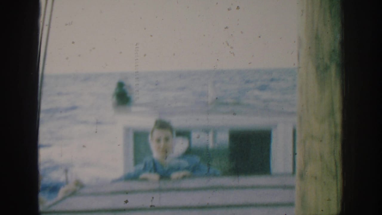 In the Rhodes 1962 boat scene, the woman faces the camera from behind the rail with the sea filling the background.