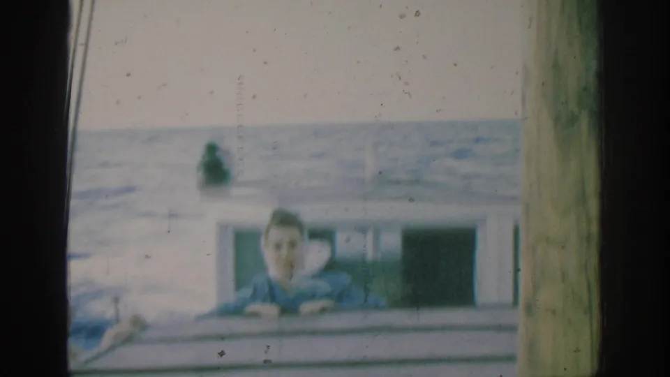 In the Rhodes 1962 boat scene, the woman faces the camera from behind the rail with the sea filling the background.