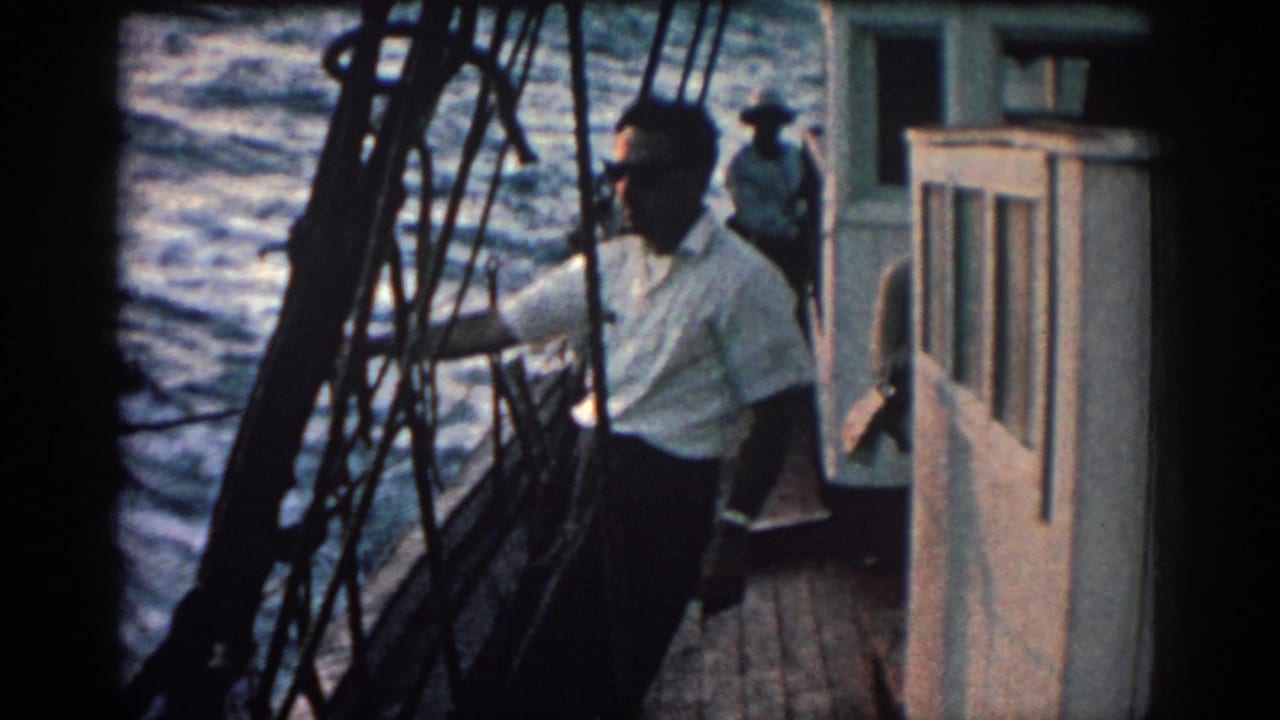 In 1962 Rhodes, Greece footage, a man stands on a boat deck near rigging and cabin windows as the sea moves behind him.